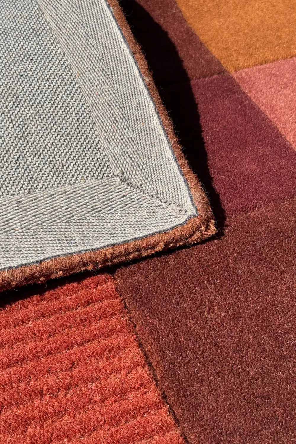 close up texture of a blockwork hand-tufted wool rug in terracotta, rust, and oxblood with ribbed and plain panels