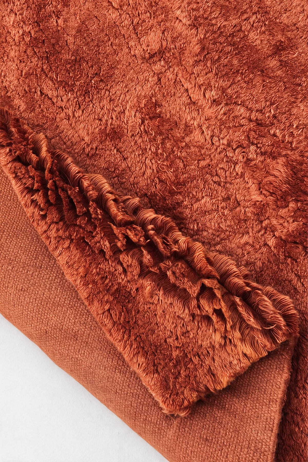 Close-up of the deep burnt orange wool pile on a JUBI hand-knotted shag rug